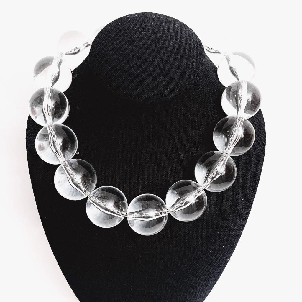 Clear acrylic bead necklace displayed on a black jewelry stand, featuring large round transparent beads that reflect light beautifully, creating a crystal‑like sparkle against a white background.