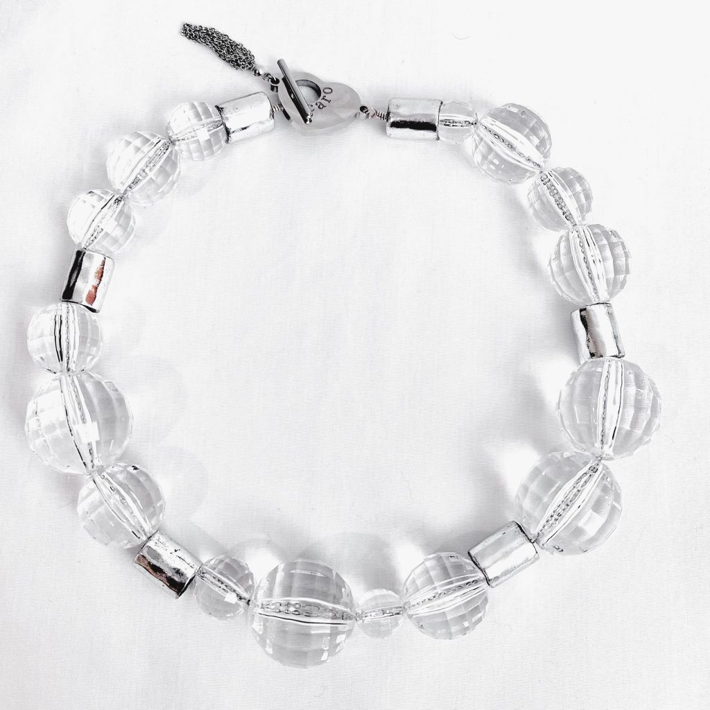 Modern clear crystal necklace featuring round faceted beads and silver cylindrical spacers with a toggle clasp, displayed on a white background to highlight its luminous and elegant design.