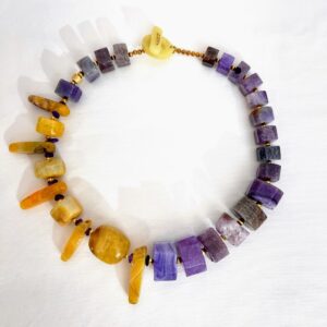 Handcrafted Purple and Yellow Agate Necklace displayed on a white background, featuring alternating rectangular and irregular gemstone beads in rich violet and golden hues. The stones are separated by small metallic spacers, highlighting their natural texture and color contrast. A round light clasp with a small engraved tag completes the design, emphasizing the necklace’s artisanal craftsmanship and vibrant elegance.