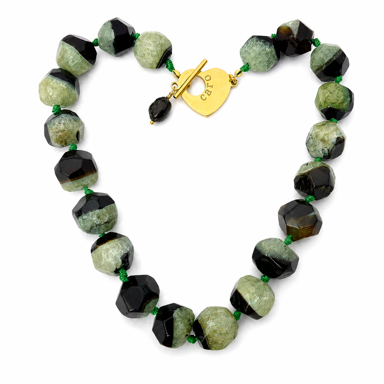 Handcrafted necklace featuring alternating faceted green and black agate stones with natural crystalline texture, connected by green knots and finished with a gold heart clasp engraved “Caro.” The design highlights organic beauty and refined craftsmanship.