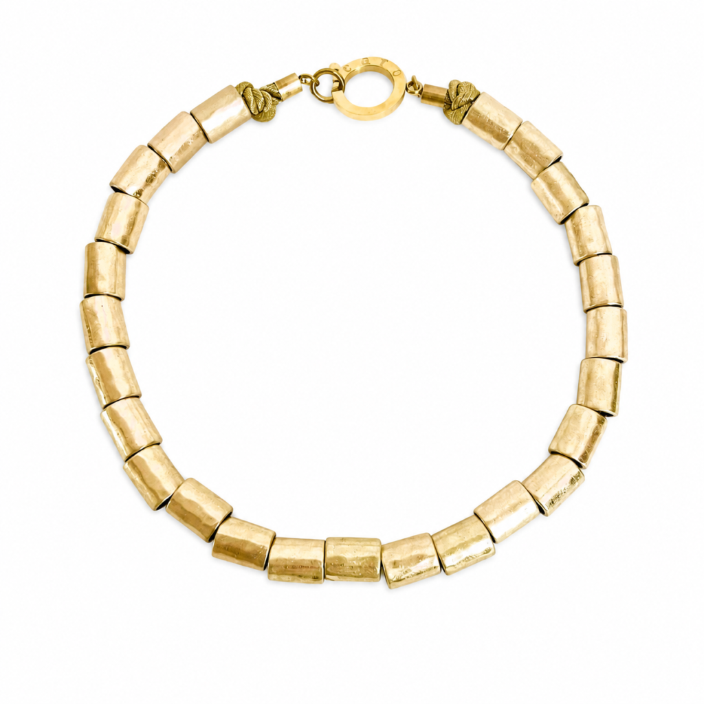Handcrafted necklace featuring cylindrical matte gold beads arranged in a uniform strand with a round gold clasp engraved “Caro.” Displayed on a white background.