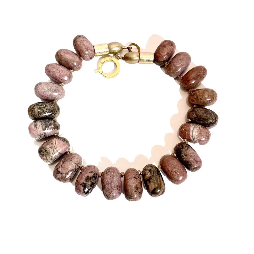 Handcrafted necklace featuring large polished Rhodonite beads in shades of rose pink with black veining, accented by gold‑tone rectangular beads and a circular clasp engraved “Caro.” Displayed on a light background.