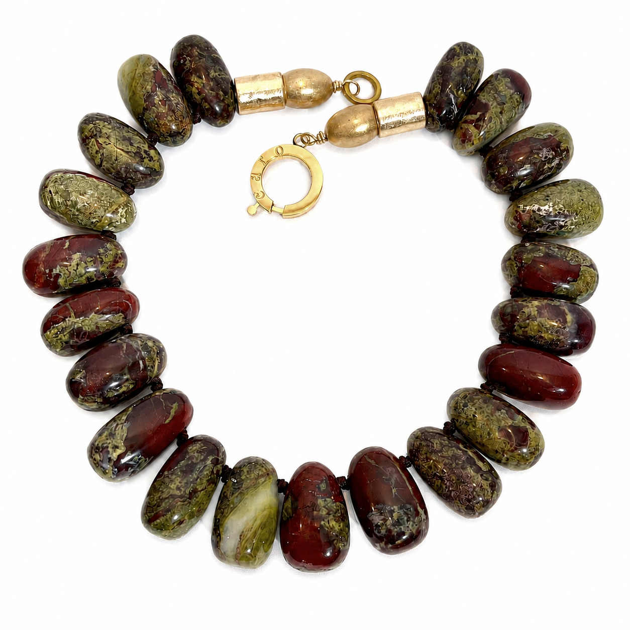 Handcrafted necklace featuring large polished Dragon Blood Jasper beads in deep green and red tones, accented by matte gold cylindrical beads and a circular clasp engraved “Caro.” Displayed on a light background.