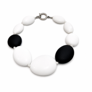 Handcrafted necklace featuring large smooth oval beads alternating between matte black and glossy white, connected by a silver circular clasp engraved “Caro.” Displayed on a white background.