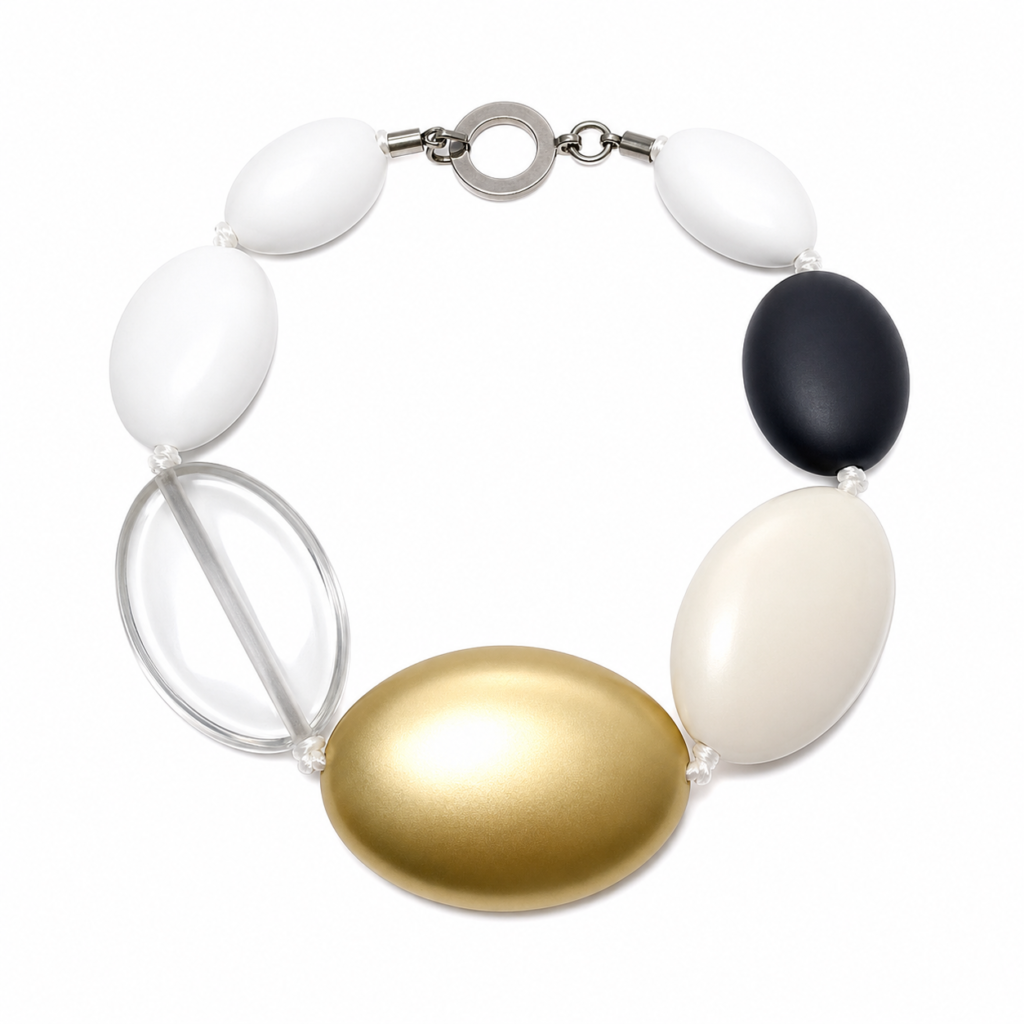 Handcrafted multi‑accent oval bead necklace featuring matte white, black, gold, and clear acrylic beads with a silver circular clasp engraved “Caro.” Displayed on a white background, highlighting its modern, sculptural design and balanced color contrast.