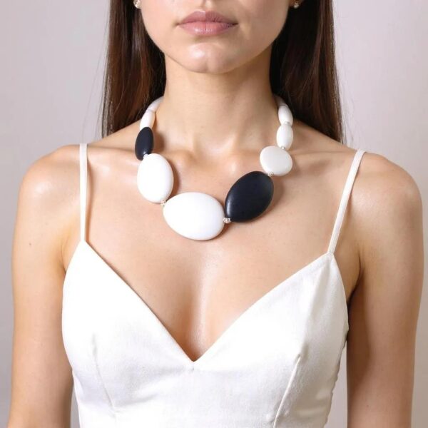 Brighten your wardrobe with the bold simplicity of the Monochrome Oval Bead Statement Necklace—a striking piece designed to add contemporary flair to your everyday style. Crafted from smooth white oval-shaped acrylic beads, this white necklace offers a clean, modern silhouette that feels sculptural yet approachable. Accented with carefully placed black beads, the design balances contrast and cohesion, creating a look that's visually impactful without being overpowering. Though chunky in form, the white necklace remains lightweight and wearable, making it the perfect companion from sunrise to sundown. Whether layered over a crisp button-down for work or styled with a casual tee for the weekend, its confident presence adapts with ease. The single-strand design provides just the right amount of drama, offering a bold aesthetic without overwhelming your outfit. Made for the fashion-forward woman who values comfort and statement-making style, this piece is as practical as it is polished. Its versatile black-and-white palette pairs effortlessly with a wide range of colors, patterns, and textures—making it a go-to accessory you’ll reach for again and again.  With its striking contrast and thoughtfully balanced proportions, the Monochrome Oval Bead Statement Necklace brings modern minimalism to life—proof that bold can also be beautifully wearable.