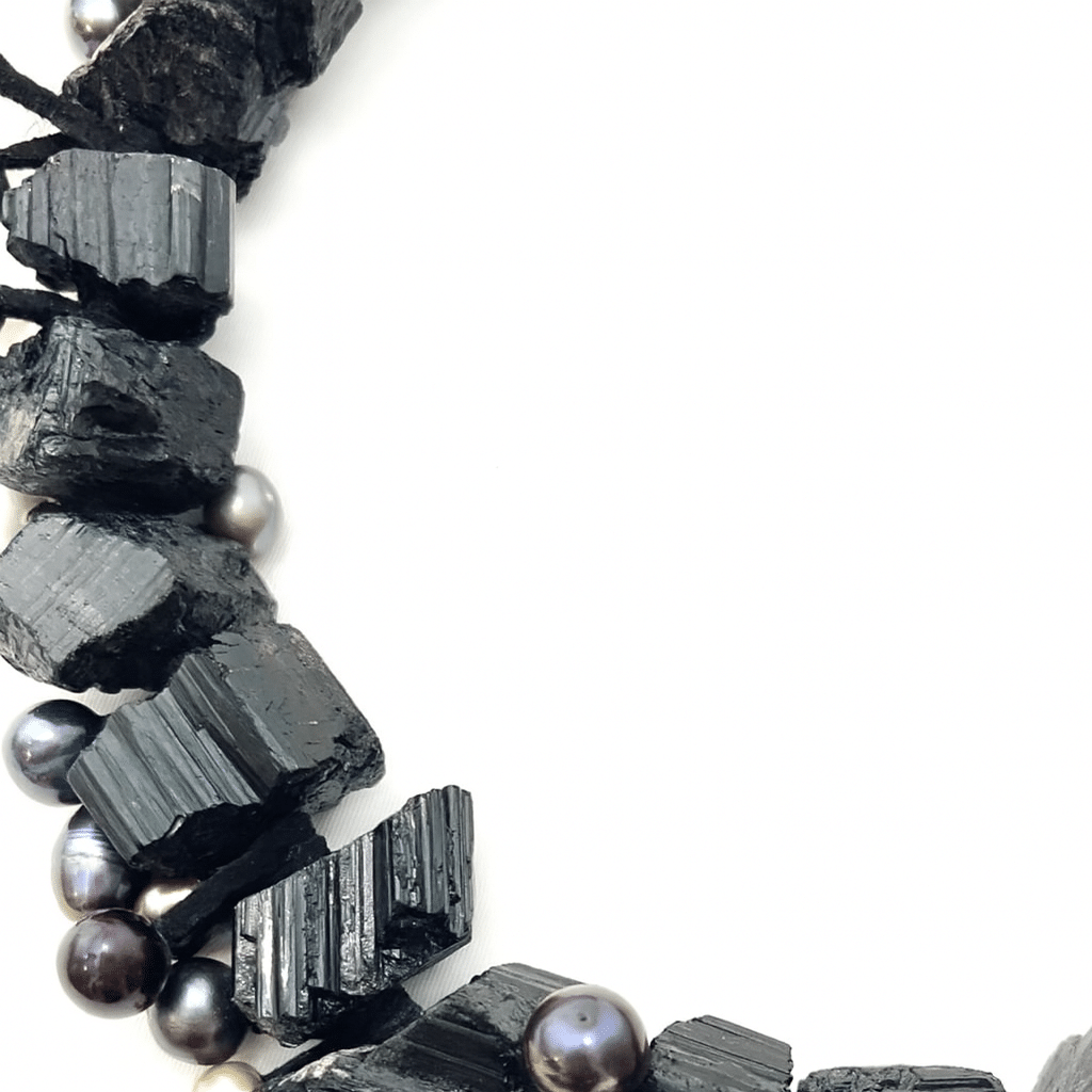 A celebration of nature, history, and personal wellness, the Black Tourmaline & Freshwater Pearl Aromatherapy Necklace is a wearable work of art crafted for the soulful and stylish. This striking black necklace features a bold yet refined combination of raw-cut black Tourmaline stones and luminous freshwater pearls—each element bringing texture, balance, and timeless elegance to the piece. Tourmaline, with its distinctive rugged finish, symbolizes grounding and protection. It’s long been revered by healers and spiritual practitioners for its energy-cleansing properties, making this necklace not only a beautiful adornment but also a meaningful talisman. The contrast between the earthy strength of Tourmaline and the smooth iridescence of pearls creates visual harmony and tactile intrigue. What sets this piece apart is its multifunctionality: the raw Tourmaline surfaces are suitable for applying essential oils, allowing you to infuse the necklace with your favorite scent for a personalized aromatic experience throughout the day.  With a heritage dating back to 1400 in Saxony, Germany, and sourced from renowned regions including Brazil, Pakistan, and the US, this necklace pays homage to the global story of Tourmaline while showcasing expert craftsmanship. For those who seek jewelry that blends beauty, history, and mindful living, this piece is a radiant expression of all three.