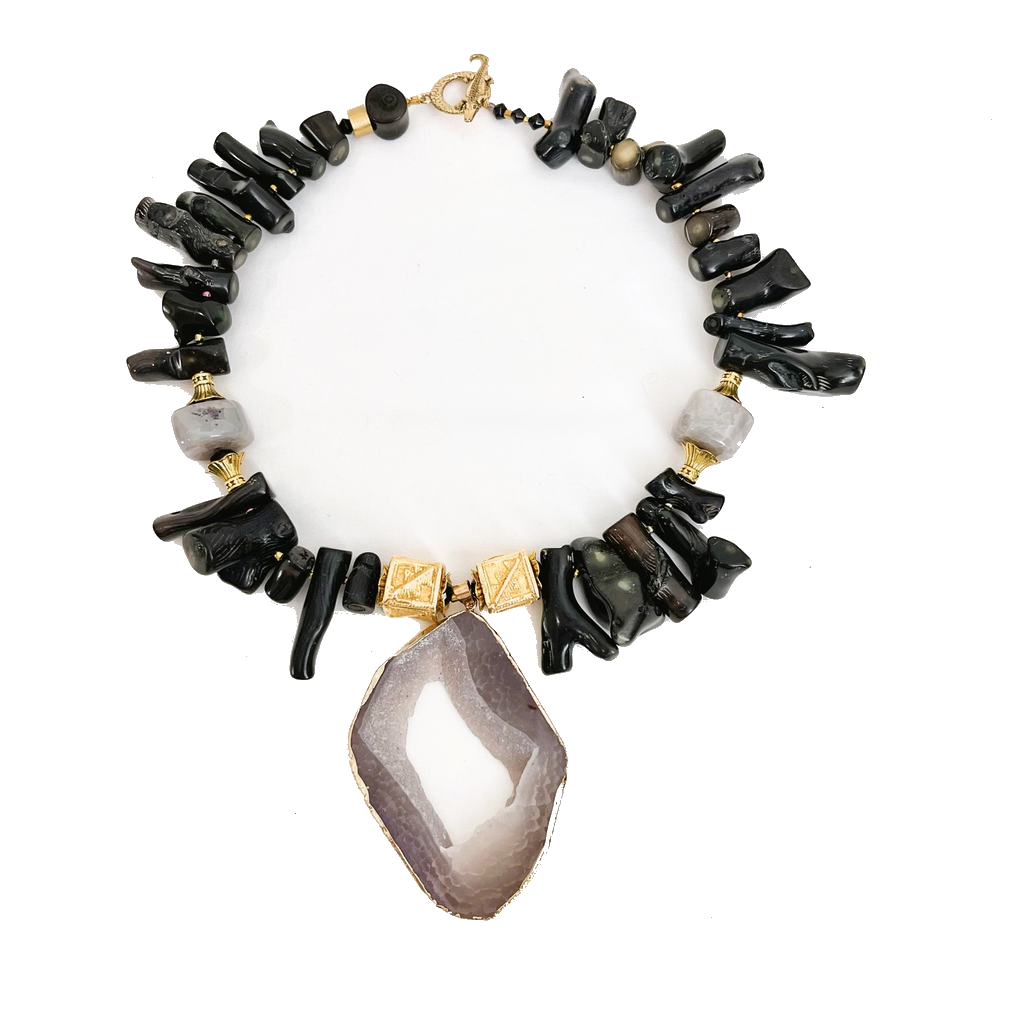 Handcrafted necklace featuring irregular black agate stones, gray accent beads, and gold‑toned geometric beads with a large sliced gray agate pendant framed in gold. Displayed on a white background, highlighting its natural textures and elegant color contrast.