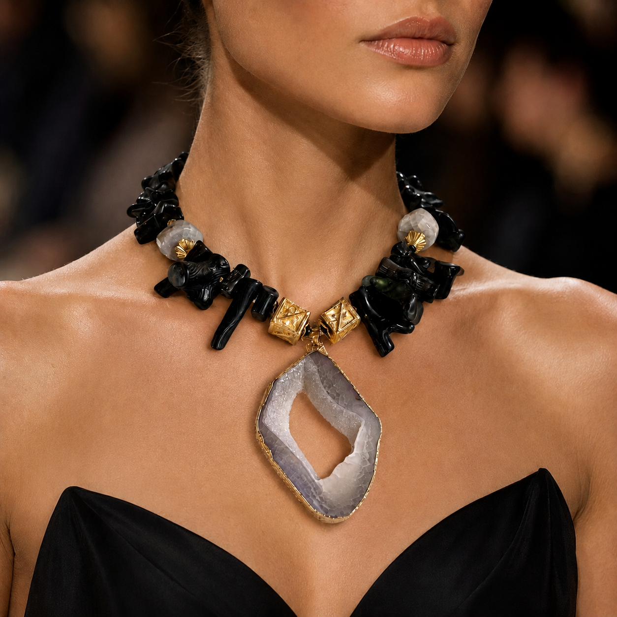 Model wearing a handcrafted Black Agate and Gold Accent Necklace featuring irregular black stones, gold‑toned beads, and a sliced gray agate pendant framed in gold. Styled with a strapless black dress, showcasing the necklace’s bold elegance and refined contrast.