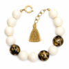 Handcrafted Ivory & Gold Tassel Necklace featuring ivory beads, black accents with gold foil leaf detailing, and a sleek gold tassel. Displayed on a white background, highlighting its elegant contrast and adjustable design.