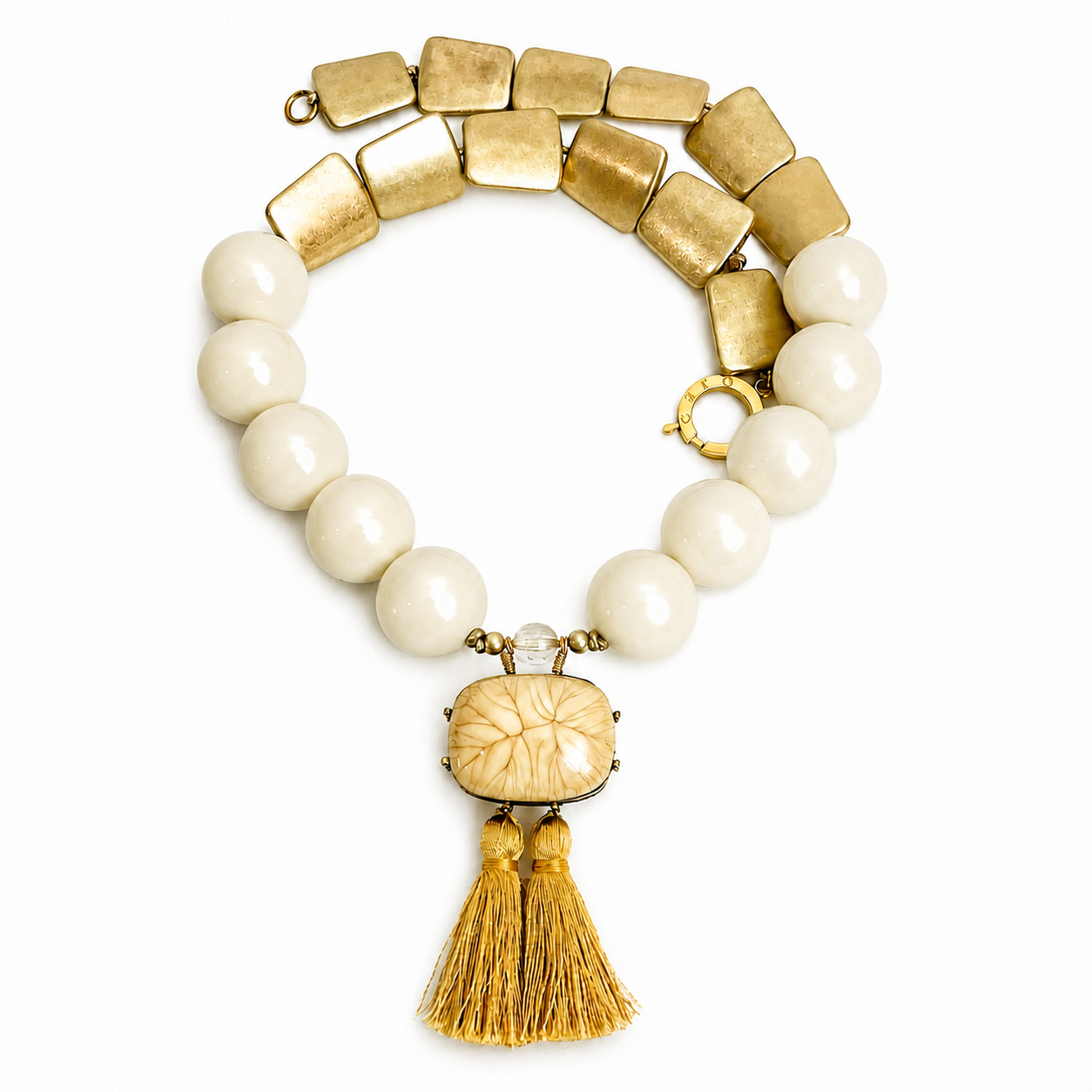 Caro Original statement necklace with ivory beads, matte gold links, and a carved centerpiece adorned with twin golden tassels.