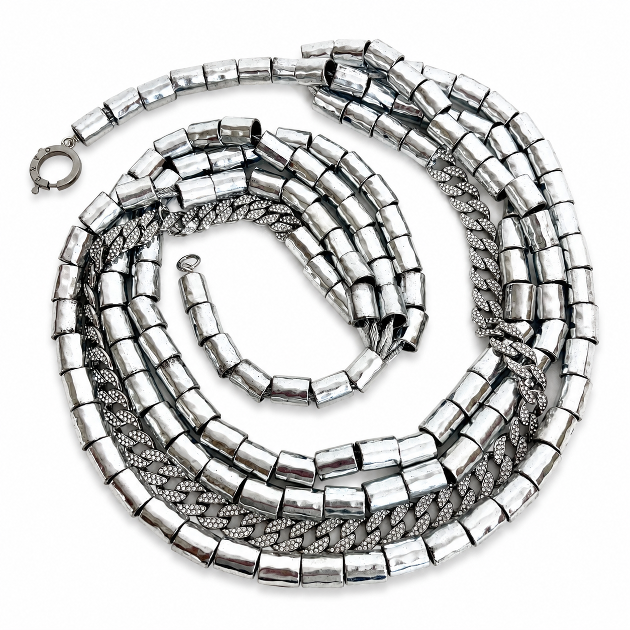 Multiple silver metallic necklaces coiled on a white background, featuring cylindrical beads and textured chain links with a reflective finish.