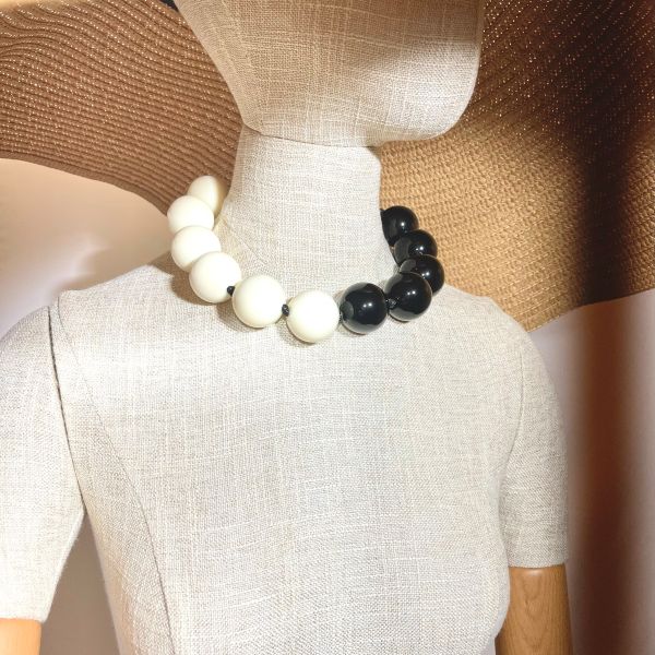Sophisticated in its simplicity, the Black & Ivory Dual-Tone Acrylic Necklace is a striking Classico accessory that effortlessly complements any wardrobe. Designed with large, knotted acrylic beads arranged in a bold half-circle of deep black and soft ivory, this Classico necklace captures the power of contrast while remaining refined and versatile. The balanced pairing of monochrome hues lends itself to endless styling possibilities—whether layered over brights, pastels, or neutrals, the necklace becomes a grounding yet eye-catching centerpiece. Its sculptural silhouette adds drama without distraction, and the generous bead size gives it presence while maintaining lightweight comfort. A true statement! Perfect for those who appreciate classico design with modern edge, the dual-color composition evokes a sense of symmetry and harmony, turning an everyday accessory into a statement of timeless taste. Wear it solo for impact or pair it with coordinating pieces for a layered look that speaks to polished versatility. From workday confidence to evening chic, the Black & Ivory Dual-Tone Acrylic Necklace adapts gracefully to your moment—proof that elegance doesn’t need excess to stand out.