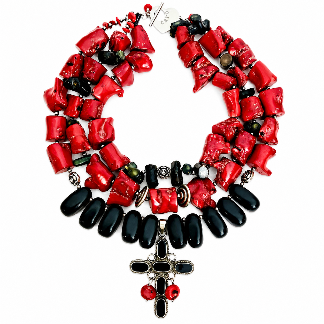 Triple‑strand statement necklace featuring large natural red coral beads and polished black obsidian stones with metallic accents, centered by a black cross pendant adorned with red coral details and a silver “Caro” tag near the clasp.