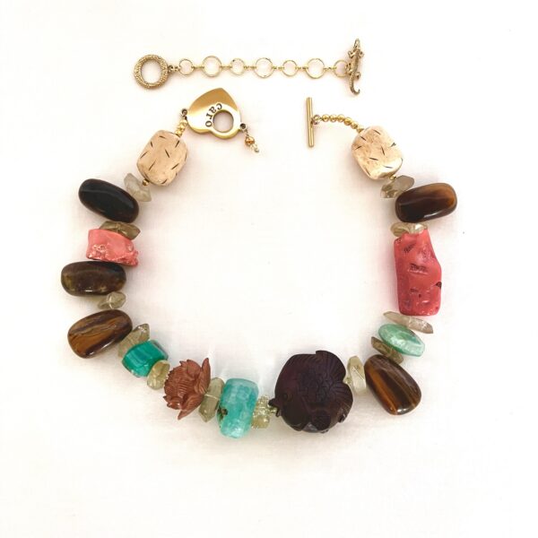 Bring nature’s symbolism to life with this captivating necklace—a stunning blend of color, texture, and cultural meaning. Measuring 17 inches with an extender that lengthens up to 20 inches, it’s crafted with intention using vibrant, all-natural materials. Every bead is different, thoughtfully chosen to spark curiosity and admiration. The hand-carved wood fish centerpiece is not just a design—it’s a symbol of abundance, prosperity, and wealth, anchoring the necklace with its spiritual significance. Surrounding it are brilliant accents: fiery orange Coral, tranquil green Agate, shimmering brown Tiger Eye, sunny yellow Quartz, and a delicately handcrafted Peachwood Lotus flower. Together, they form a harmonious mosaic of prosperity that celebrates the beauty of contrast. This piece invites conversation and admiration, its vivid colors and meaningful elements making it as expressive as it is elegant. Whether you wear it for personal empowerment, prosperity inspiration, or artistic flair, this necklace stands out with purpose. Each stone and bead tells its own story, from natural origin to symbolic depth. It’s not just jewelry—it’s wearable intention, designed to captivate and connect. Ideal for lovers of unique artisan pieces, spiritual symbolism, and bold style that doesn’t shy away from speaking its truth.