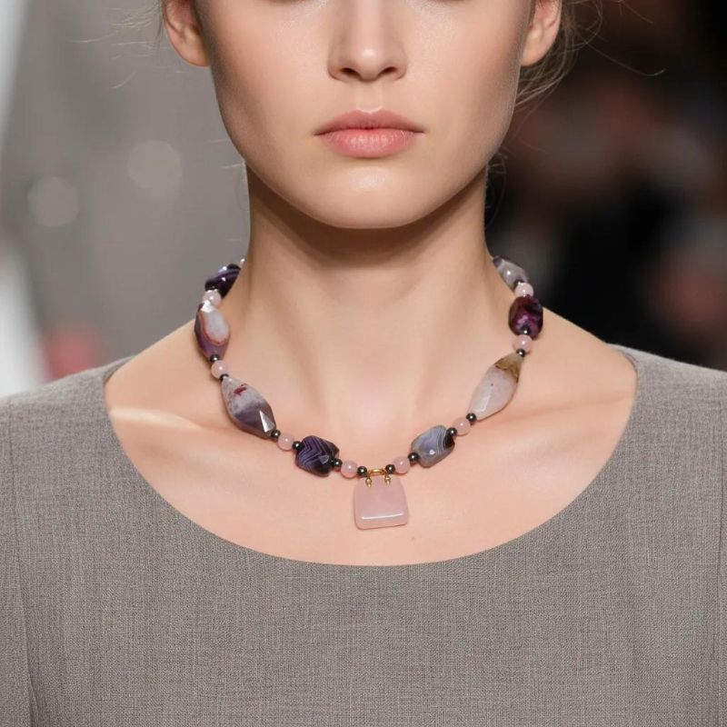 Delicate yet expressive, this sweet pink necklace is a refined celebration of soft tones and intricate natural beauty. Designed for those who appreciate quiet elegance, it features the captivating Botswana Agate—renowned for its subtle banding and harmonious blend of pink and gray hues. These calming tones are mirrored in the pairing of blush-pink Quartz and cool gray Pearls, lending the necklace an air of romantic sophistication. Though petite in size, the pink necklace offers a wealth of detail. The Botswana Agate’s intricate patterns provide visual depth, while each element contributes texture and grace. A charming pink Agate handbag pendant serves as a playful accent that elevates the minimalist silhouette. Adding a final note of luxury, a striking gold charm completes the design with a polished touch. Measuring with comfort and style in mind, this pink necklace is ideal for layering or wearing solo to draw subtle attention. It’s the perfect statement for soft-spoken fashionistas who favor expressive accessories with personality and intention. Whether gifted or chosen for oneself, this necklace brings together modern sensibility and natural artistry in one graceful composition—proof that small treasures often carry the biggest stories.