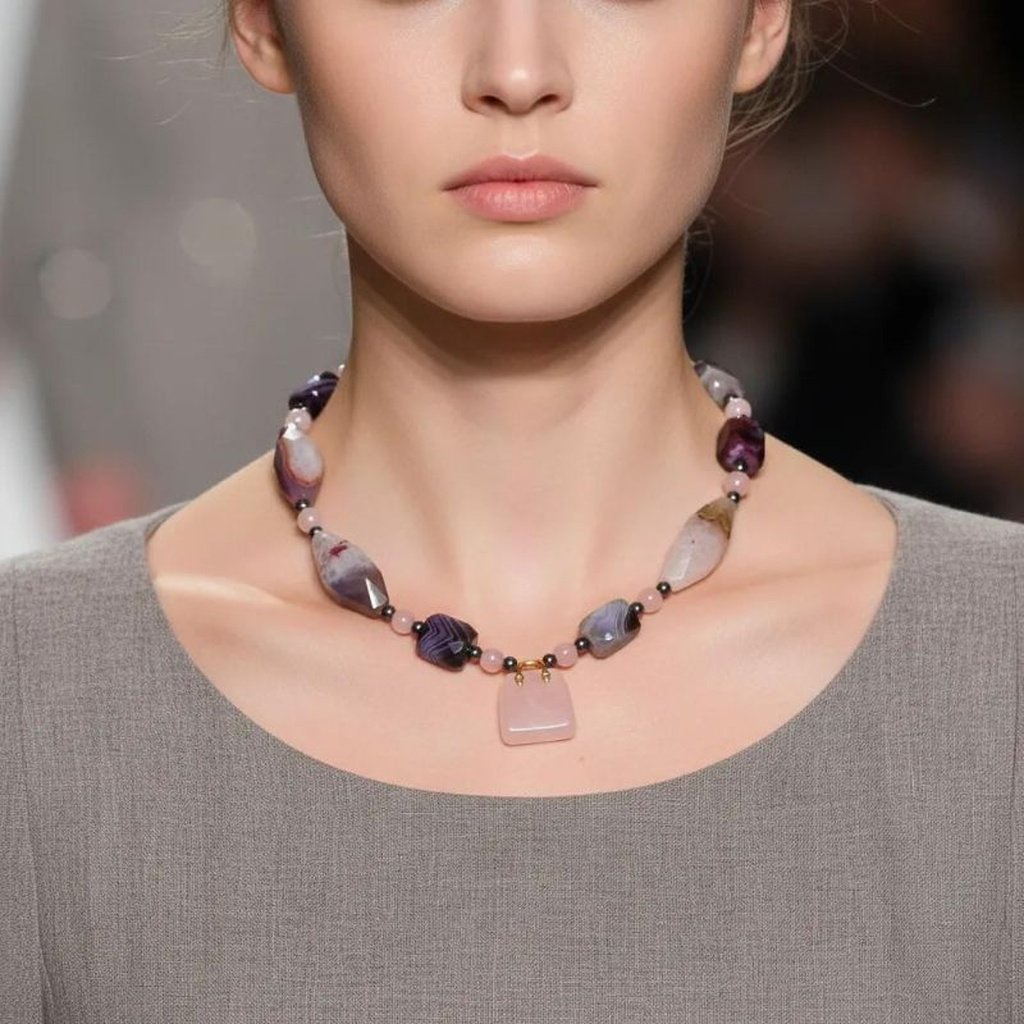 Model wearing a handcrafted Pink Necklace with Botswana Agate, blush Quartz, and gray Pearls, centered by a pink handbag‑shaped pendant, styled with a gray dress.