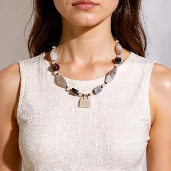 Delicate yet expressive, this sweet pink necklace is a refined celebration of soft tones and intricate natural beauty. Designed for those who appreciate quiet elegance, it features the captivating Botswana Agate—renowned for its subtle banding and harmonious blend of pink and gray hues. These calming tones are mirrored in the pairing of blush-pink Quartz and cool gray Pearls, lending the necklace an air of romantic sophistication. Though petite in size, the pink necklace offers a wealth of detail. The Botswana Agate’s intricate patterns provide visual depth, while each element contributes texture and grace. A charming pink Agate handbag pendant serves as a playful accent that elevates the minimalist silhouette. Adding a final note of luxury, a striking gold charm completes the design with a polished touch. Measuring with comfort and style in mind, this pink necklace is ideal for layering or wearing solo to draw subtle attention. It’s the perfect statement for soft-spoken fashionistas who favor expressive accessories with personality and intention. Whether gifted or chosen for oneself, this necklace brings together modern sensibility and natural artistry in one graceful composition—proof that small treasures often carry the biggest stories.