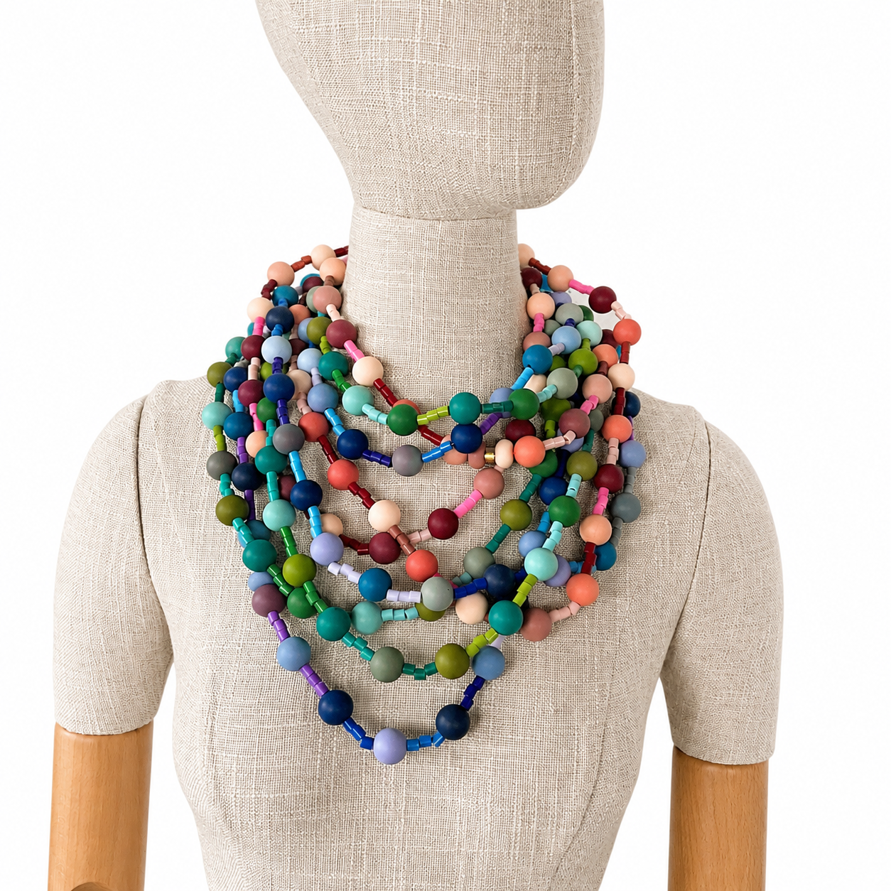 Mannequin wearing multiple layered long necklaces made of round and cylindrical silicone beads in a wide range of colors—blue, green, pink, peach, purple, and beige—creating a vibrant, stacked look against a neutral fabric background.
