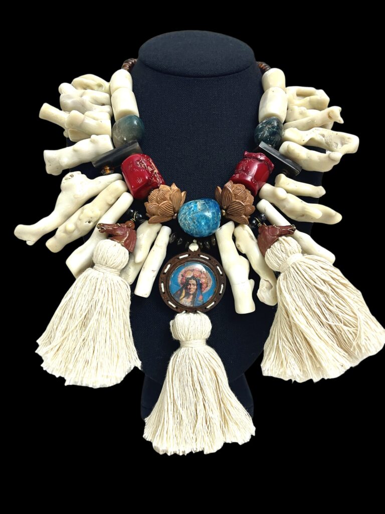 A true masterpiece of wearable art, this captivating necklace merges Italian traditional style with artisanal brilliance and exotic charm. Measuring 19 inches (46 cm) and weighing 19 ounces, it commands attention with its sculptural silhouette and bold presence—perfect for collectors and connoisseurs alike. At its heart lies a distinctive wood medallion, framed by a dynamic blend of Coral, Labradorite, and Apatite—natural stones celebrated for their vibrant energy and grounding beauty. Elegant tassels cascade gracefully from the medallion, adding movement and layered depth. Brass horses and bone elements weave through the design, enriching its texture and evoking elegance infused with Italian symbolic weight. More than a necklace, it’s an Italian exhibition piece you can wear—a fusion of culture, nature, and artisan skill. The Italian motifs stand out as conversation starters, perfect for gallery strolls or sophisticated evenings. Whether paired with minimalist apparel to highlight its rich detail or incorporated into a more bohemian ensemble, this statement accessory transforms any look into a story. With every bead and tassel, it celebrates heritage, intention, and individuality. Let it be the centerpiece of your collection—a design that speaks volumes and captivates with grace.