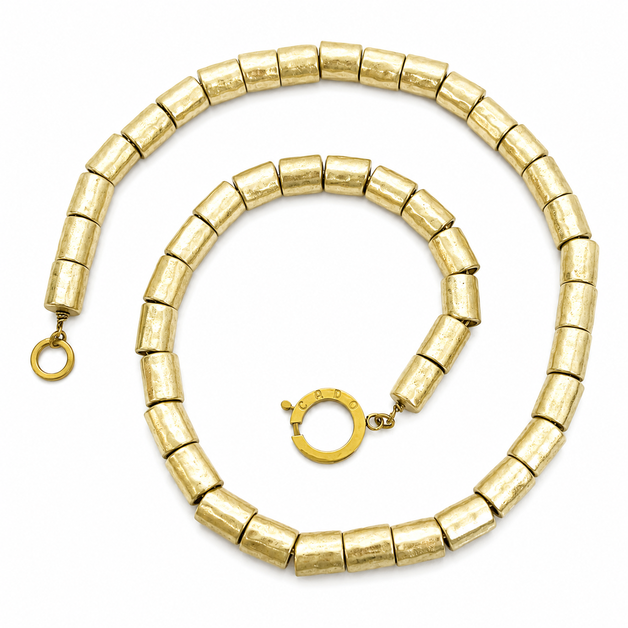Long necklace composed of cylindrical antique gold beads with a textured finish, arranged in a continuous strand and secured with a round gold clasp engraved “Caro.” Displayed on a white background.