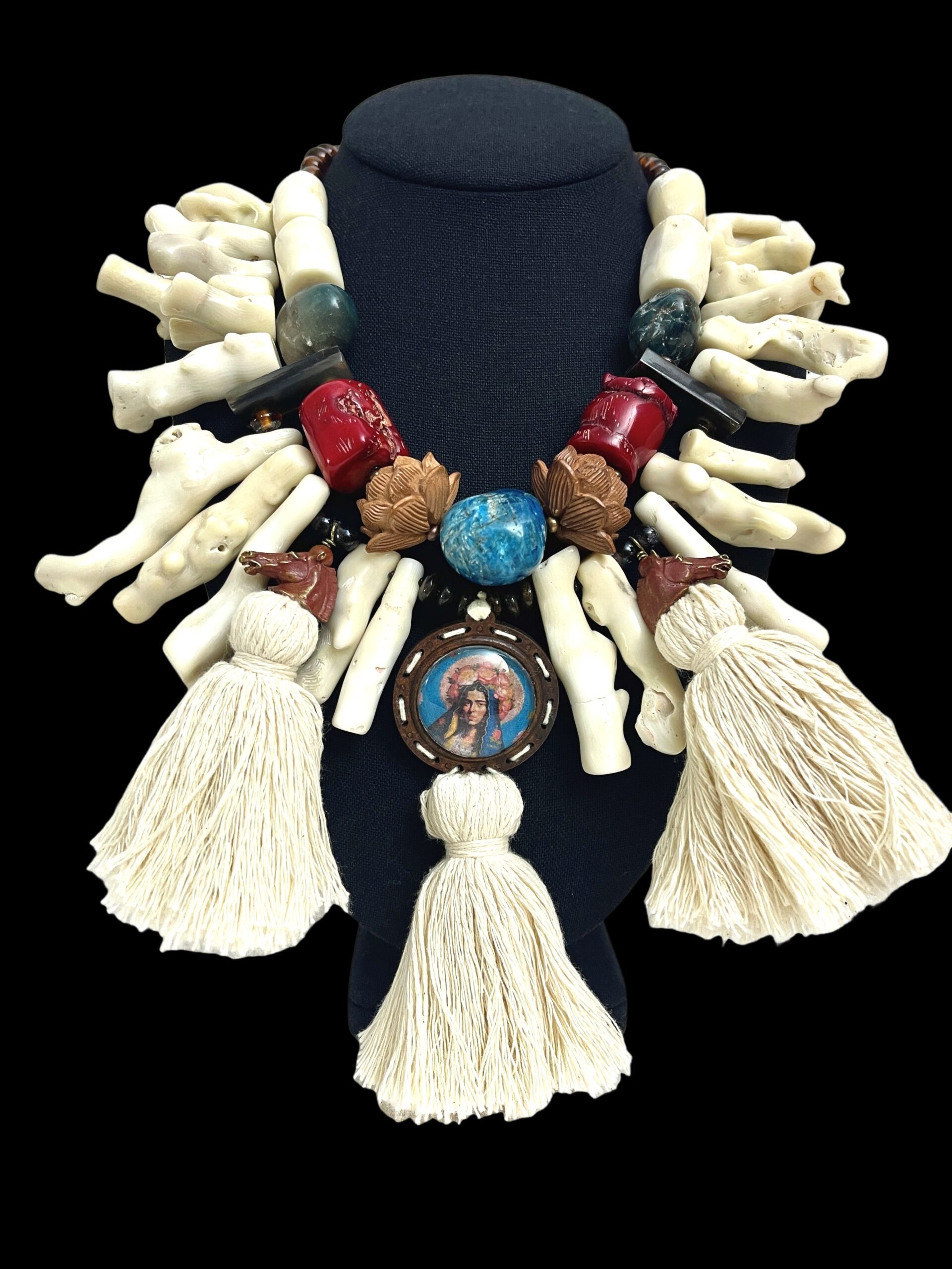 Handcrafted Italian statement necklace displayed on a black bust, featuring large white coral branches, red and green stones, carved brown floral beads, and three cream tassels. At the center hangs a circular medallion with a painted portrait framed by decorative elements.