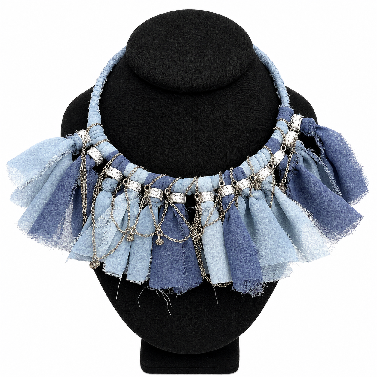 Handcrafted statement necklace displayed on a black bust, featuring alternating strips of light and dark blue frayed fabric arranged in a ruffled pattern. Silver beads and delicate chains drape across the front, adding shimmer and movement to the design.