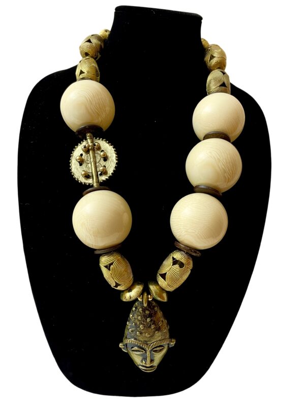 A large African mask pendant with extra-large ivory color beads, coconut shells, and brass beads.  A statement one-of-a-kind necklace measuring 29IN/27OZ.  The rich colors and textures make it easy to wear.  African masks are worn to mark life stages, natural cycles, and celebrations.