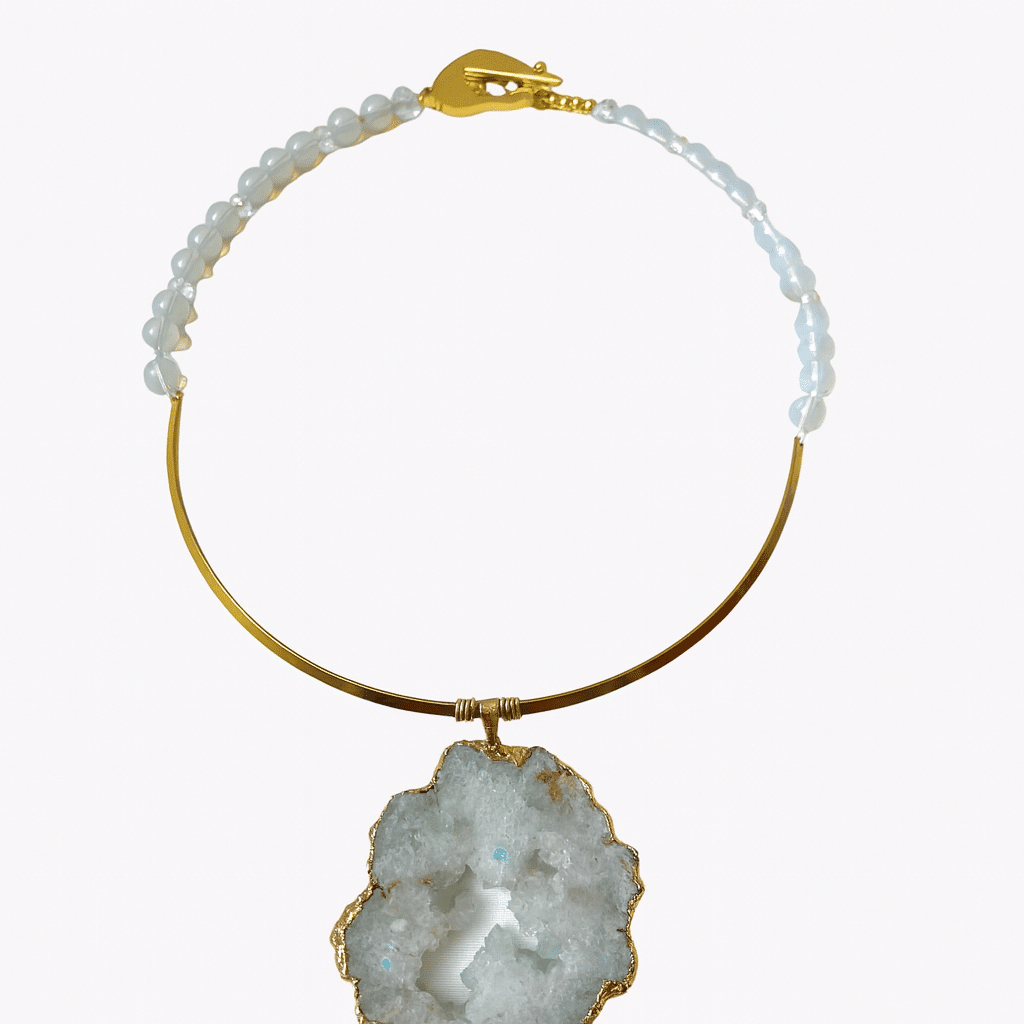 Elevate your look and spirit with this exquisite sliced crystal necklace—a harmonious blend of beauty, meaning, and sensory elegance. Measuring 24 inches and weighing a substantial yet comfortable 6 ounces, this piece is more than a striking accessory; it’s a meaningful talisman infused with intention. The necklace features a raw crystal rock, artfully sliced and framed in warm gold, revealing the stone’s organic textures and natural brilliance. Each angle catches the light in subtle ways, reflecting both simplicity and drama. Delicate white beads accentuate the design with a soft contrast, lending a timeless charm that complements both casual and formal attire. Beyond its visual allure, the pendant holds deeper significance. In mystic traditions, stones like this are revered for their calming energy, believed to resonate with the wearer and promote well-being. For an intimate ritual, apply a favorite scent oil directly to the stone, allowing its porous surface to gently diffuse the fragrance throughout the day. It’s a wearable sanctuary, merging beauty and tranquility with every breath. Ideal for those who seek a fusion of aesthetic refinement and spiritual intention, this necklace is a piece to be seen, felt, and experienced. Let it center your style and soothe your soul.