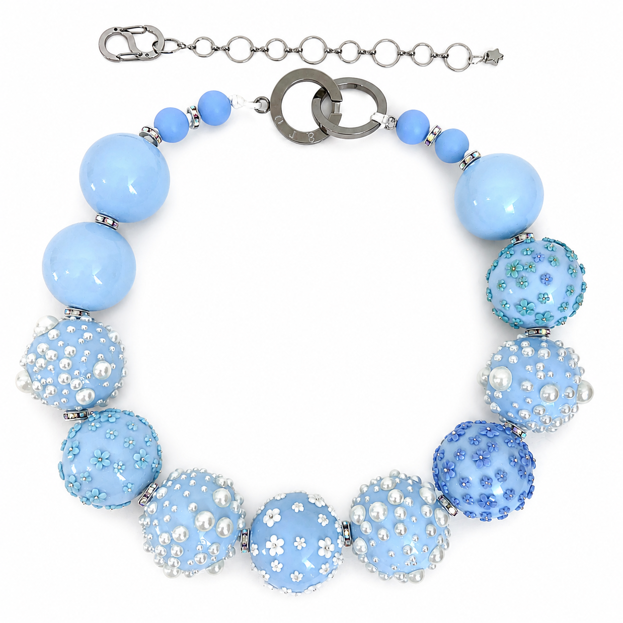 Statement necklace composed of large glossy baby-blue beads alternating with textured beads adorned with tiny white flowers and pearl-like accents. The necklace features a silver chain extender and clasp for adjustable length.
