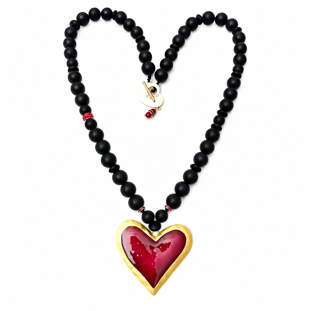 Statement necklace composed of matte black beads arranged in a graduated pattern, featuring a large glossy red heart pendant outlined in gold. The necklace is displayed on a white background, with the beads forming a heart shape to highlight the pendant.