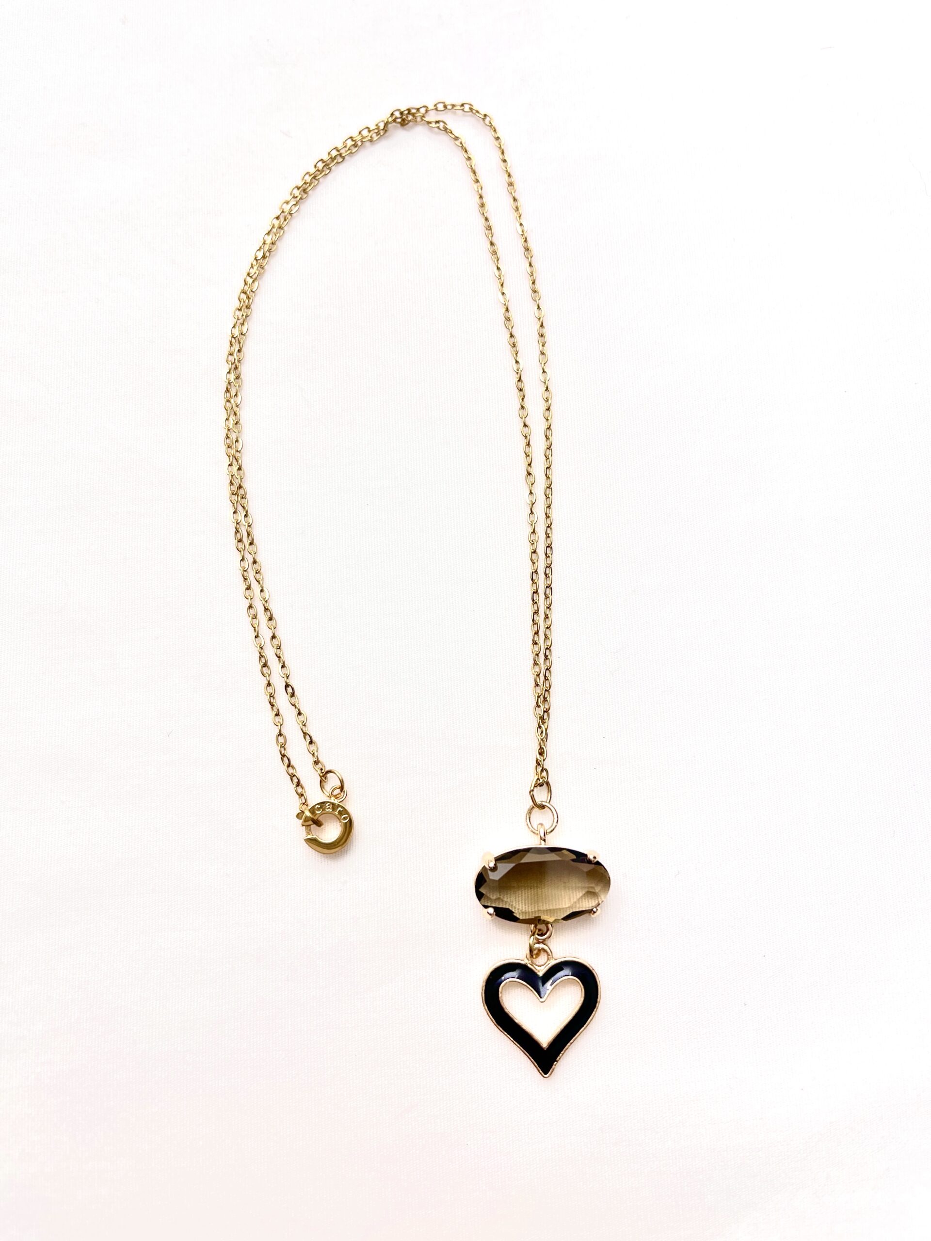 Gold chain necklace featuring an oval smoky gemstone and a hollow heart pendant outlined in black enamel. The design blends modern elegance with a subtle vintage touch.