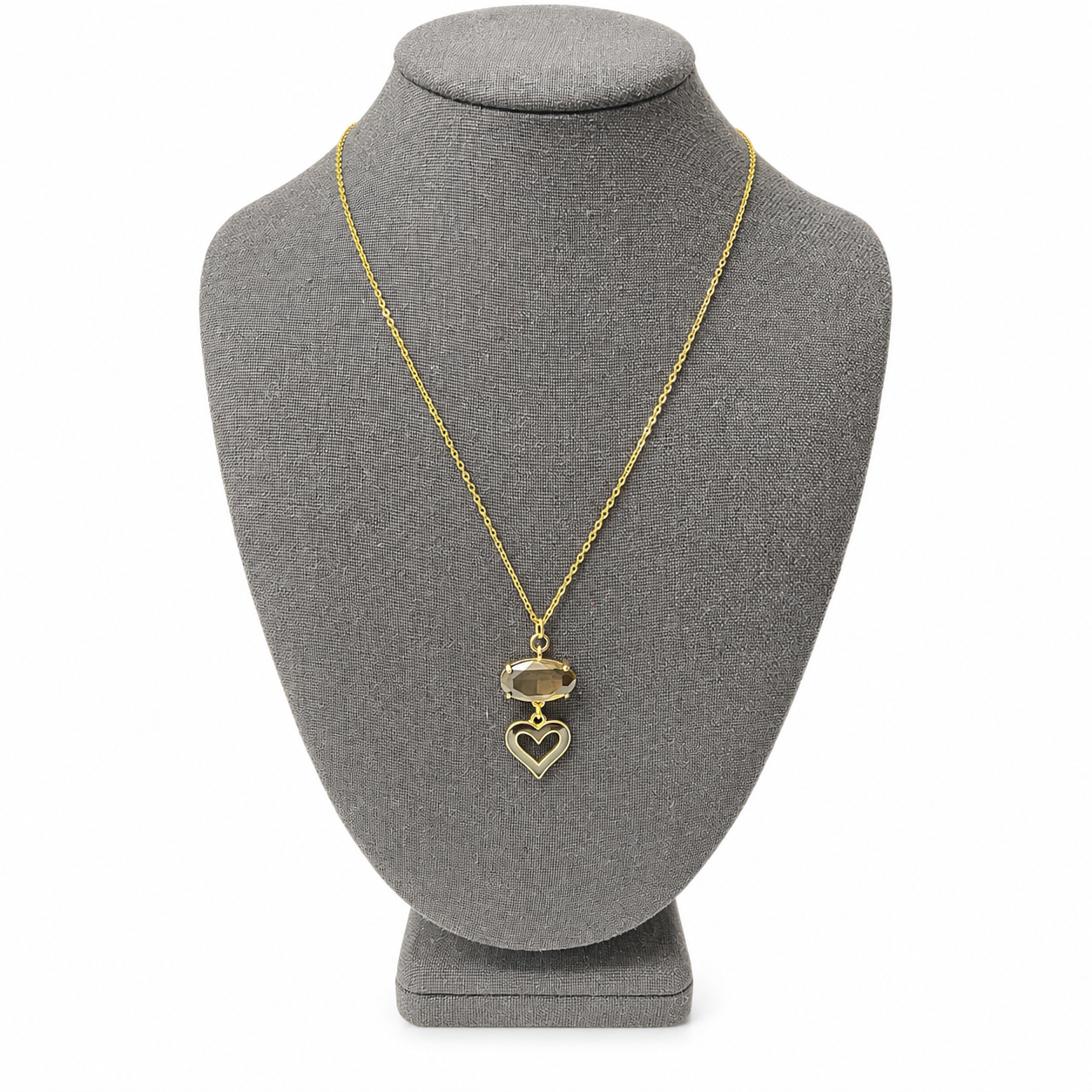 Gold necklace displayed on a gray jewelry bust, showcasing an oval smoky crystal and a black‑outlined open heart pendant. The piece exudes sophistication and timeless charm.