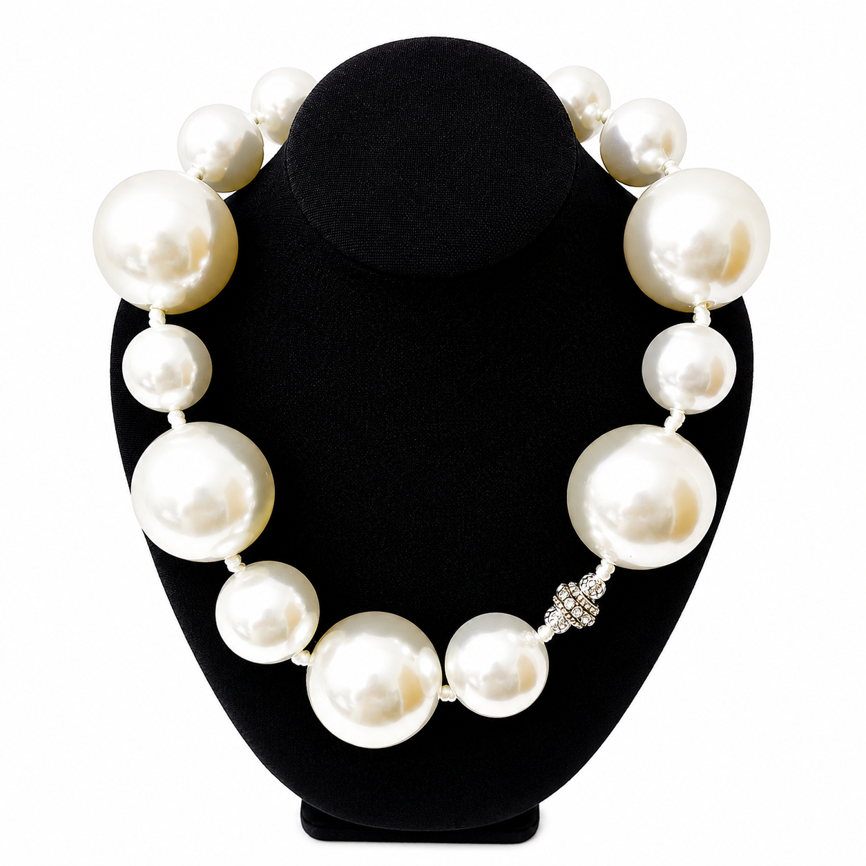Elegant necklace displayed on a black velvet stand, featuring oversized glossy white pearls arranged in a graduated pattern. A small rhinestone-encrusted accent adds sparkle among the lustrous pearls.