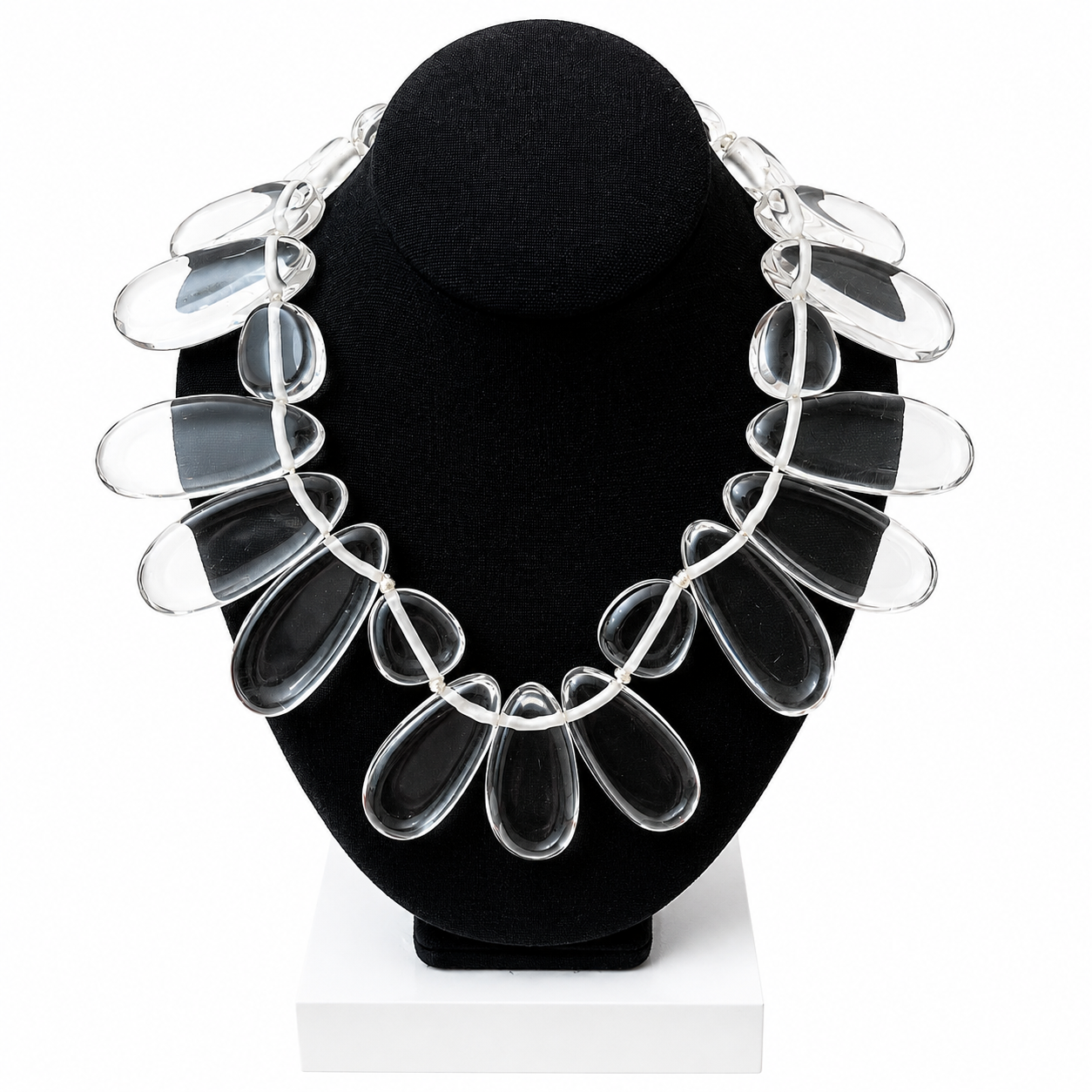 Clear necklace displayed on a black jewelry bust. The design consists of large, flattened teardrop-shaped beads made of transparent material, symmetrically arranged to resemble flower petals.