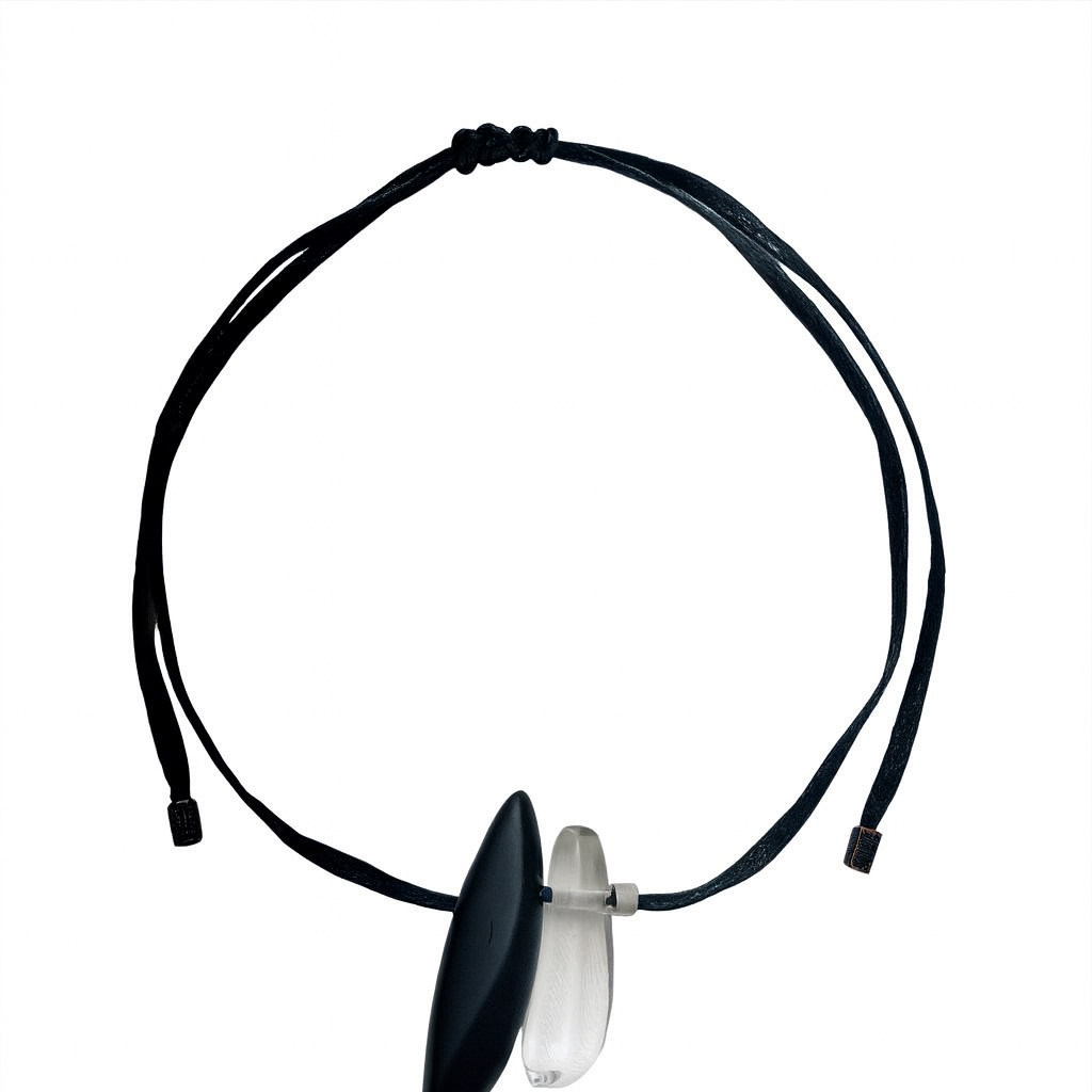 Minimalist necklace featuring a thin black cotton cord with two pendants—one matte black and one translucent clear. The pendants are elongated and smooth, creating a modern contrast between opacity and transparency.