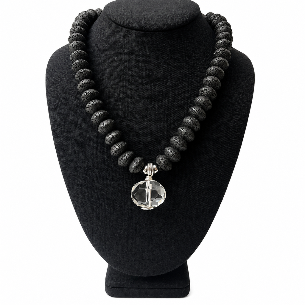 Necklace composed of matte black lava beads arranged in a display featuring a single faceted clear crystal pendant at the center. The clasp includes a silver chain extender for adjustable length.