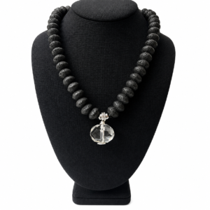 Necklace composed of matte black lava beads arranged in a display featuring a single faceted clear crystal pendant at the center. The clasp includes a silver chain extender for adjustable length.