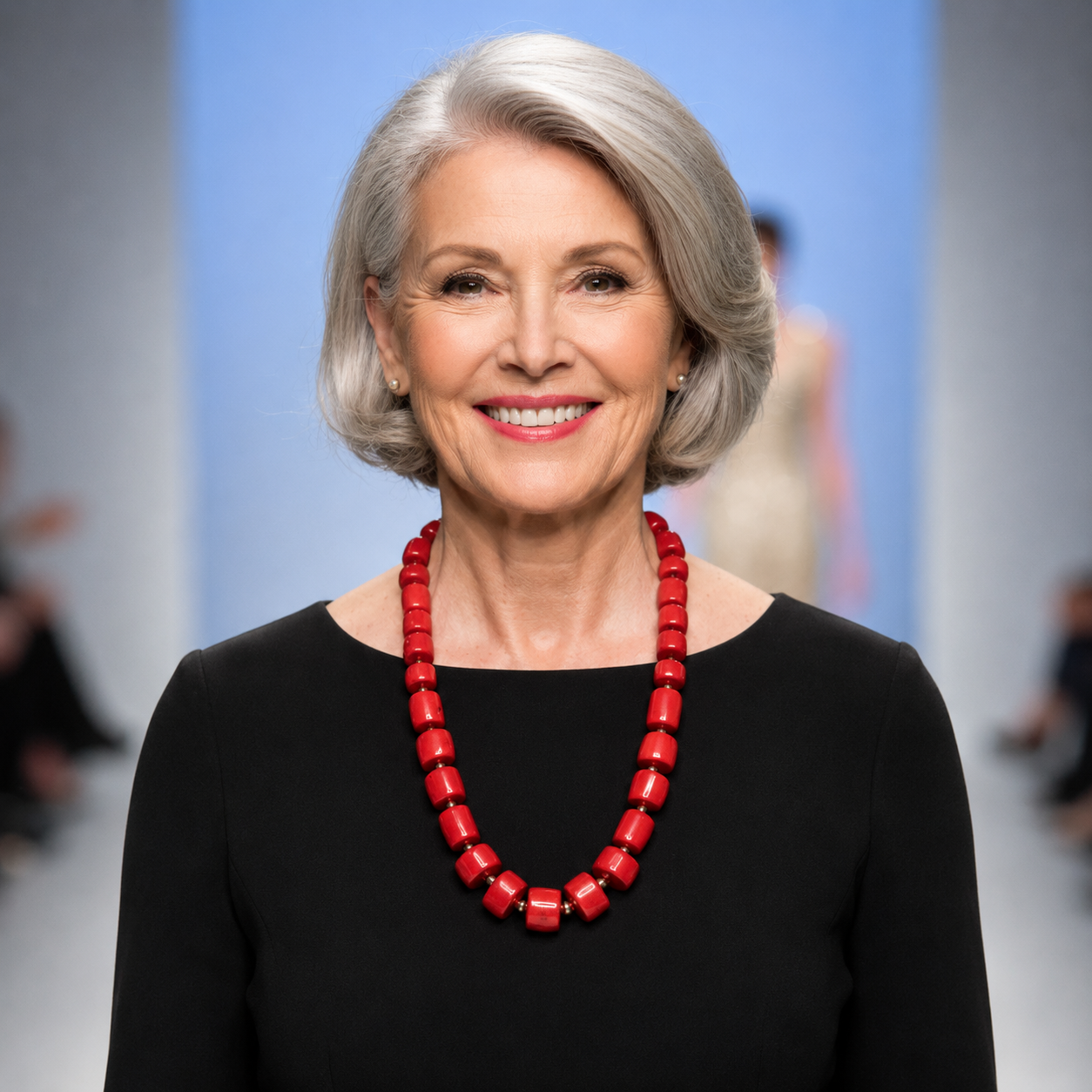 Model wearing a long red coral bead necklace with gold accents over a black dress. The vibrant red beads contrast elegantly against the dark fabric, creating a bold and sophisticated look.