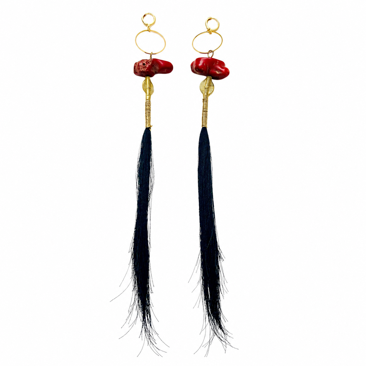 Pair of long statement earrings featuring irregular red coral stones at the top, gold accents, and extra-long black tassels that extend downward. The design combines bold color contrast with fluid movement.