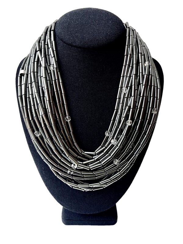 🌒 A statement in sophistication and strength, the Hematite Necklace embodies bold design with a shimmering touch. Handcrafted with 24 gleaming strands, this piece offers a dynamic combination of texture, light, and history. Measuring 19 inches at its shortest and extending up to 24 inches, its generous weight of 20 ounces enhances its luxurious presence while remaining comfortably wearable. Each strand is adorned with a faceted crystal, lending brilliance and movement to the overall silhouette. The lustrous silver tone of Hematite creates an elegant backdrop, contrasting beautifully with the sparkle of the crystals and the deep tones of the Onyx toggle clasp. This adjustable clasp allows the necklace to be styled in multiple ways—flat across the collarbone, twisted for volume, or crossed for an avant-garde edge. Whether worn with the clasp in front or back, every arrangement offers a new mood and visual rhythm. Historically, Hematite held symbolic significance—it was worn as a talisman by English warriors, believed to safeguard those wounded in battle. Its inclusion here infuses the necklace with quiet power and cultural depth. Perfect for collectors of meaningful jewelry and lovers of sculptural elegance, this piece invites admiration for its craftsmanship and versatility. The final whisper of Hematite completes its story—resilient, radiant, and unapologetically bold.