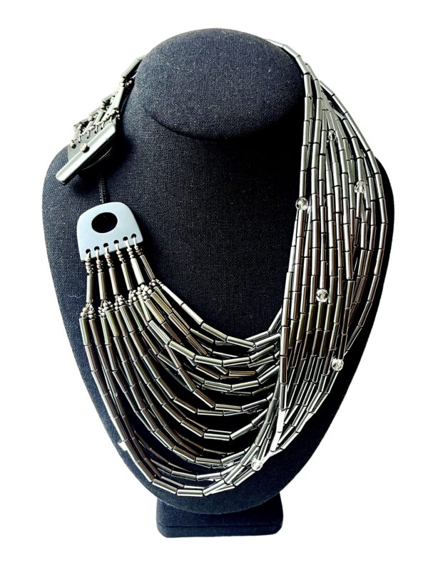 🌒 A statement in sophistication and strength, the Hematite Necklace embodies bold design with a shimmering touch. Handcrafted with 24 gleaming strands, this piece offers a dynamic combination of texture, light, and history. Measuring 19 inches at its shortest and extending up to 24 inches, its generous weight of 20 ounces enhances its luxurious presence while remaining comfortably wearable. Each strand is adorned with a faceted crystal, lending brilliance and movement to the overall silhouette. The lustrous silver tone of Hematite creates an elegant backdrop, contrasting beautifully with the sparkle of the crystals and the deep tones of the Onyx toggle clasp. This adjustable clasp allows the necklace to be styled in multiple ways—flat across the collarbone, twisted for volume, or crossed for an avant-garde edge. Whether worn with the clasp in front or back, every arrangement offers a new mood and visual rhythm. Historically, Hematite held symbolic significance—it was worn as a talisman by English warriors, believed to safeguard those wounded in battle. Its inclusion here infuses the necklace with quiet power and cultural depth. Perfect for collectors of meaningful jewelry and lovers of sculptural elegance, this piece invites admiration for its craftsmanship and versatility. The final whisper of Hematite completes its story—resilient, radiant, and unapologetically bold.