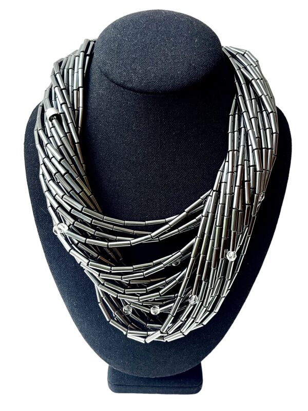 🌒 A statement in sophistication and strength, the Hematite Necklace embodies bold design with a shimmering touch. Handcrafted with 24 gleaming strands, this piece offers a dynamic combination of texture, light, and history. Measuring 19 inches at its shortest and extending up to 24 inches, its generous weight of 20 ounces enhances its luxurious presence while remaining comfortably wearable. Each strand is adorned with a faceted crystal, lending brilliance and movement to the overall silhouette. The lustrous silver tone of Hematite creates an elegant backdrop, contrasting beautifully with the sparkle of the crystals and the deep tones of the Onyx toggle clasp. This adjustable clasp allows the necklace to be styled in multiple ways—flat across the collarbone, twisted for volume, or crossed for an avant-garde edge. Whether worn with the clasp in front or back, every arrangement offers a new mood and visual rhythm. Historically, Hematite held symbolic significance—it was worn as a talisman by English warriors, believed to safeguard those wounded in battle. Its inclusion here infuses the necklace with quiet power and cultural depth. Perfect for collectors of meaningful jewelry and lovers of sculptural elegance, this piece invites admiration for its craftsmanship and versatility. The final whisper of Hematite completes its story—resilient, radiant, and unapologetically bold.
