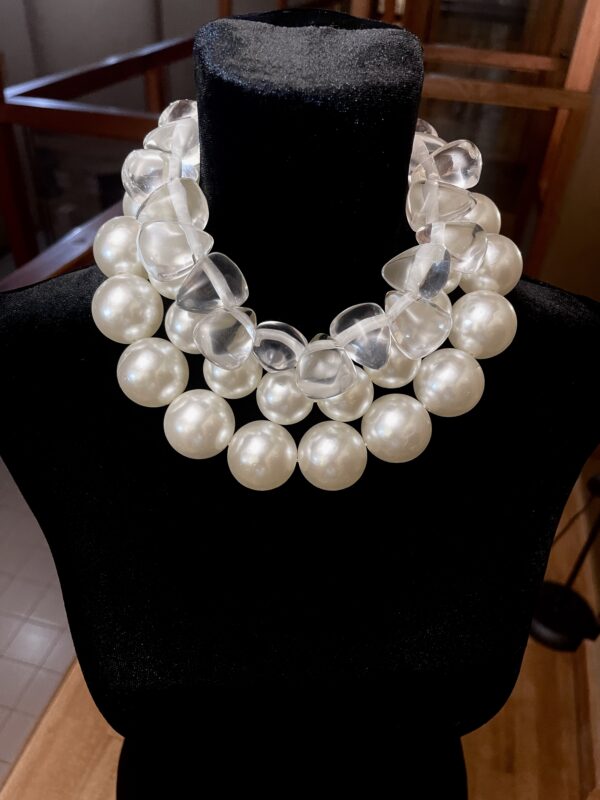 A set of 2 strands of medium-sized simulation pearls, with a separate choker necklace of one clear resin, tooth-shaped clear beads. You can wear the set or wear one or the other. The clear beads necklace contrasts the pearls' formality but also brings out the shine of the beads. The combination of styles is a unique statement for day or night. The necklace includes an extension to elongate both necklaces as a set or only one. This item sells as a set. The clear beads choker measures 16 IN/5 OZ. The double-strand necklace measures 17 IN/ 10 OZ Extension up to 5 IN A set 16 IN/15 OZ