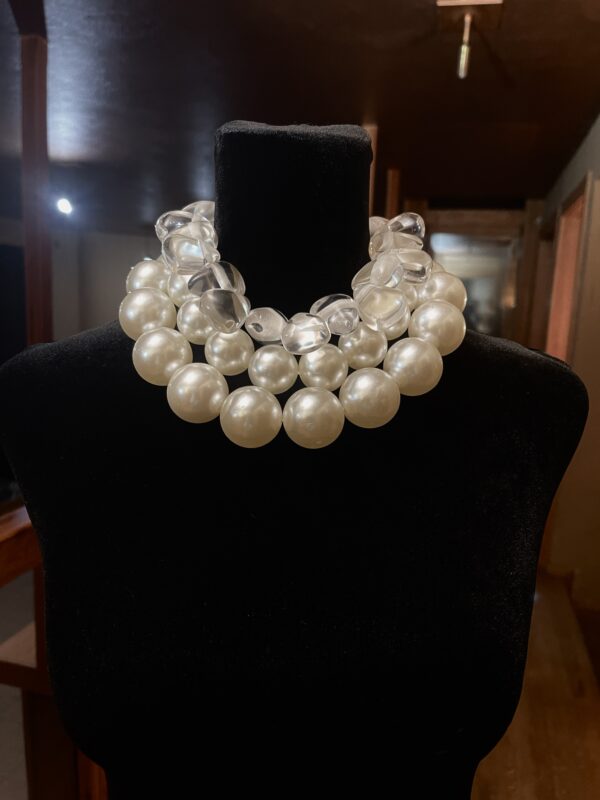 A set of 2 strands of medium-sized simulation pearls, with a separate choker necklace of one clear resin, tooth-shaped clear beads. You can wear the set or wear one or the other. The clear beads necklace contrasts the pearls' formality but also brings out the shine of the beads. The combination of styles is a unique statement for day or night. The necklace includes an extension to elongate both necklaces as a set or only one. This item sells as a set. The clear beads choker measures 16 IN/5 OZ. The double-strand necklace measures 17 IN/ 10 OZ Extension up to 5 IN A set 16 IN/15 OZ