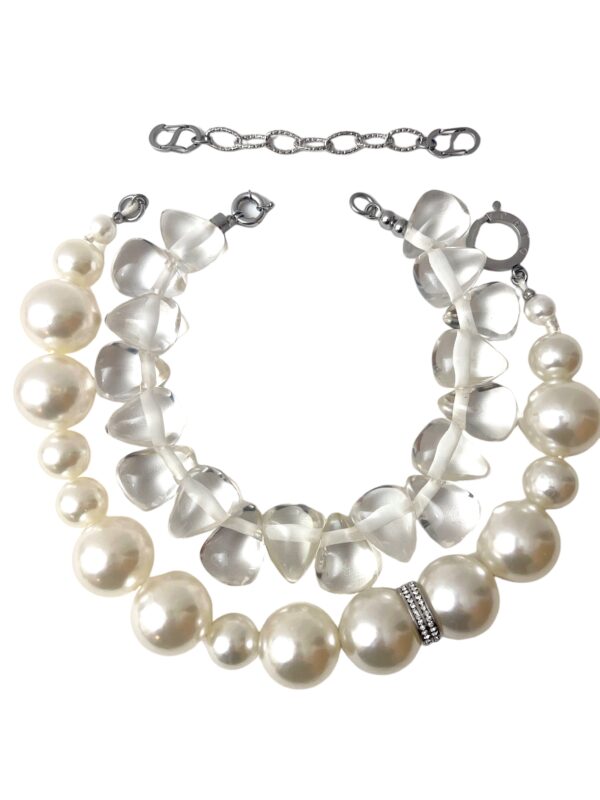 A set of 2 necklaces. One medium-sized simulation pearls, one choker necklace of resin, tooth-shaped clear beads. You can wear the set or wear one or the other. The clear beads necklace contrasts the pearls' formality but also brings out the shine of the beads. The combination of styles is a unique statement for day or night. The necklace includes an extension to elongate both necklaces as a set or only one. This item sells as a set. The clear beads choker measures 15 IN/5 OZ. The pear beads necklace measures 19 IN/6 OZ. Extension up to 5 IN. A set 19 IN/11 OZ