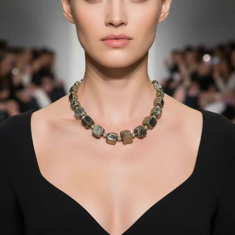 A bold expression of elemental geometry, this necklace and earring set showcases the raw elegance of natural silver Pyrite in its unpolished form. Each cube-like bead reveals the mineral’s intrinsic architecture—right-angled faces born from slow, stable crystallization, where atoms align to minimize surface energy. This phenomenon gives Pyrite its signature metallic luster and geometric precision, a marvel of nature’s quiet engineering. The necklace spans 20 inches and weighs 11 ounces, offering a substantial presence that feels both grounded and refined. Gold-toned spacer beads punctuate the silver Pyrite, adding warmth and contrast to the cool, industrial sheen. A circular toggle clasp completes the piece with vintage flair. The matching earrings echo the necklace’s design, featuring a single Pyrite bead suspended from lever-back hooks—simple, yet striking. This set is a tribute to the beauty of structure and imperfection. The unpolished surfaces catch light in unexpected ways, revealing subtle textures and tonal shifts that polished stones often conceal. Ideal for those who appreciate jewelry with depth and story, this ensemble invites conversation and admiration. Whether worn as a statement or layered with softer pieces, it celebrates the power of the unpolished—raw, radiant, and unapologetically bold.