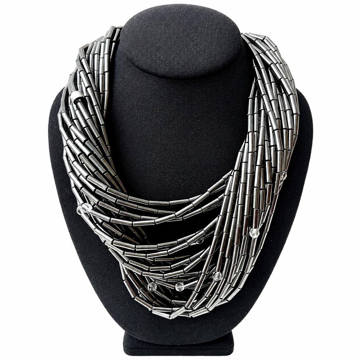 Close-up of the Hematite Necklace displayed on a dark mannequin bust. The necklace features 24 strands of metallic hematite tubes interspersed with small faceted crystals, creating a layered, shimmering effect. A silver-toned toggle clasp adds a sculptural finish.