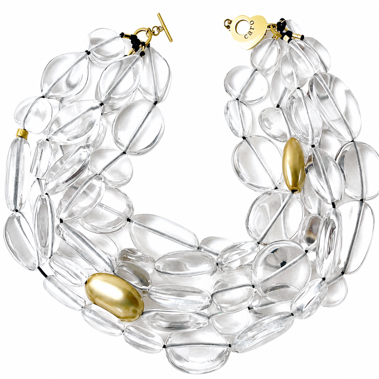 Multi-strand statement necklace composed of clear oval resin beads with a few large gold accents. The transparent beads create a layered, fluid texture, while the gold elements add warmth and contrast. The necklace features a gold toggle clasp and a small heart-shaped charm engraved with “Caro.”