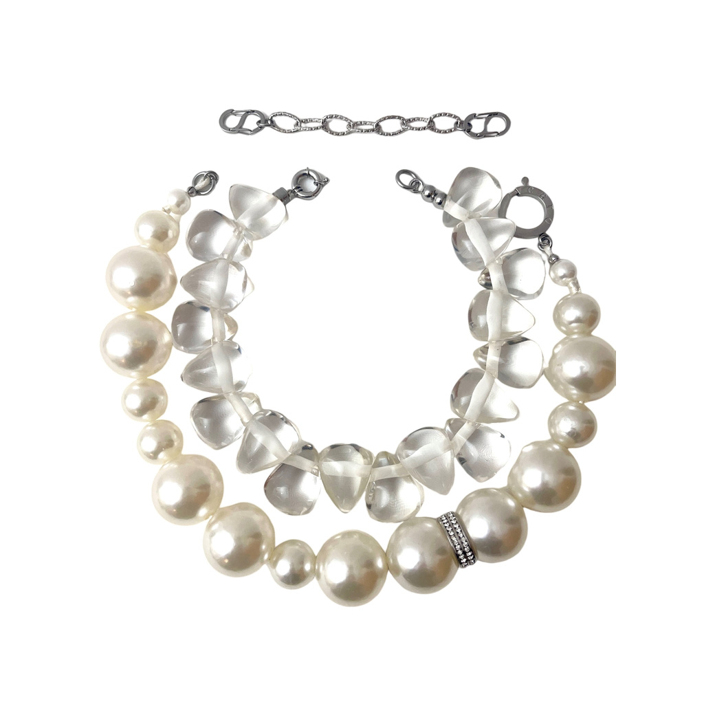 Two necklaces displayed together: one featuring large, lustrous white pearls arranged in a graduated pattern with a small rhinestone-accented ring, and the other composed of translucent, frosted resin beads shaped like cones. Both pieces have silver clasps and an adjustable chain extender, showcasing a blend of classic and modern design.